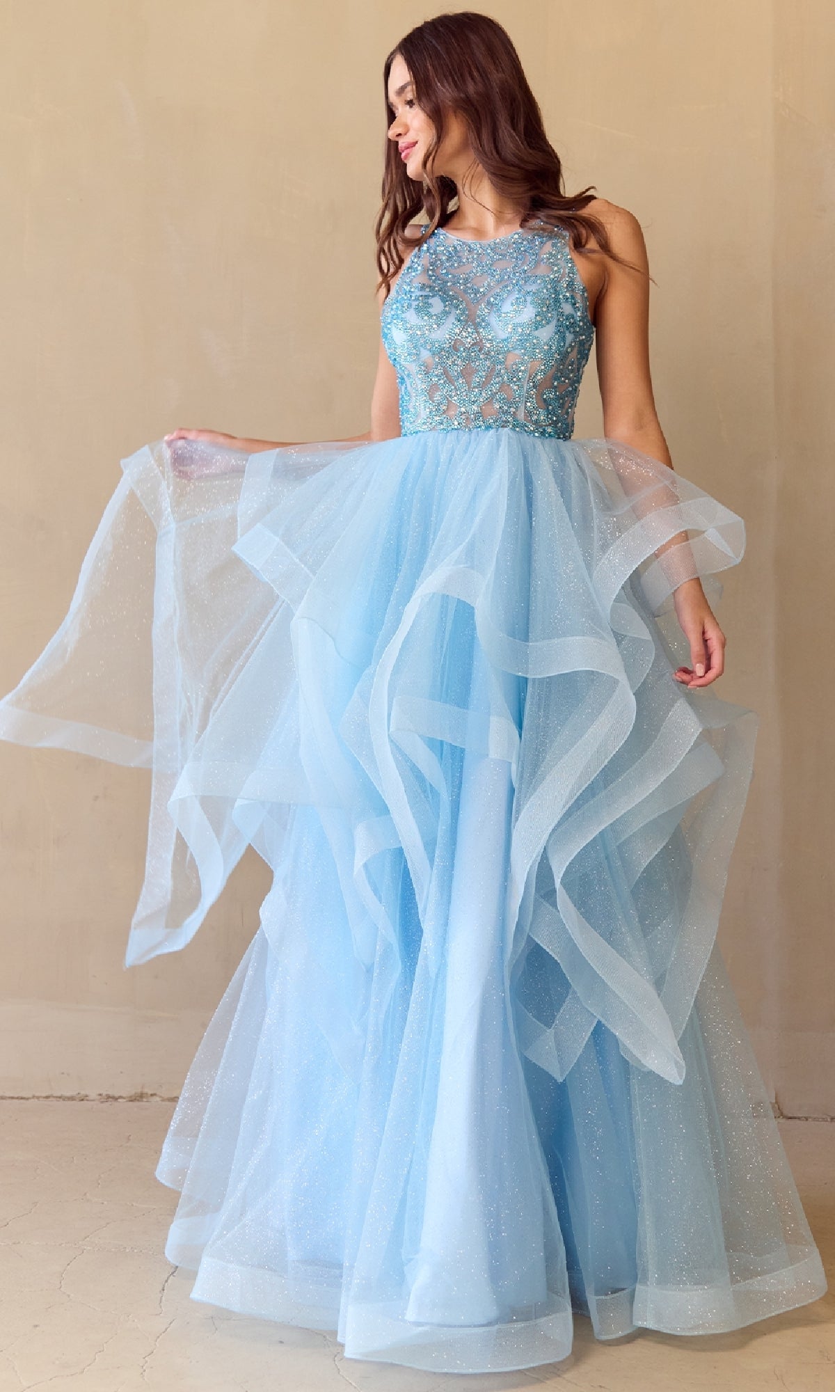 Woman wearing a light blue glitter tulle prom ball gown with a layered skirt on a beige background