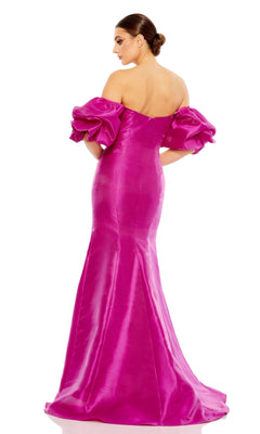 A woman faces away, wearing the Mac Duggal 50677 Off-the-Shoulder Long Gala Gown—a bright pink formal dress with voluminous ruffle sleeves and a fitted silhouette.