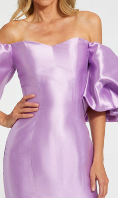 A woman poses with one hand on her hip in the Mac Duggal 50677 Off-the-Shoulder Long Gala Gown, featuring a shiny lavender fabric, mermaid silhouette, and voluminous puff sleeves.
