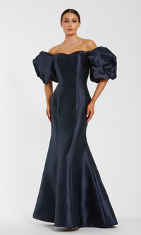 A woman wears the Mac Duggal 50677 Off-the-Shoulder Long Gala Gown in dark navy, featuring a fitted mermaid silhouette with dramatic puff sleeves and a flared hem, standing against a plain light background.