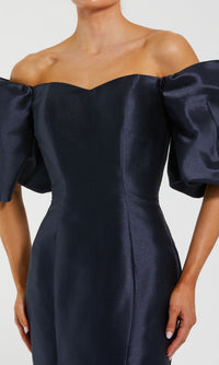 A woman in the Mac Duggal 50677 Off-the-Shoulder Long Gala Gown, featuring dark blue satin, voluminous puff sleeves, a fitted bodice, and a mermaid silhouette.