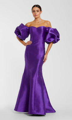 A woman poses against a plain background in the Mac Duggal 50677 Off-the-Shoulder Long Gala Gown—an elegant, floor-length purple mermaid dress featuring dramatic puff sleeves.
