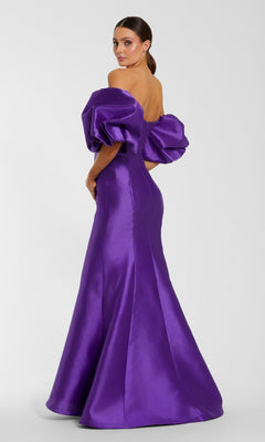 A woman stands against a plain background, looking over her shoulder in the Mac Duggal 50677 Off-the-Shoulder Long Gala Gown, featuring dramatic puff sleeves and a shiny purple mermaid silhouette.