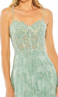 A woman in the Mac Duggal 50735 Long Formal Dress—a floor-length, light green gown with floral embroidery and thin spaghetti straps.