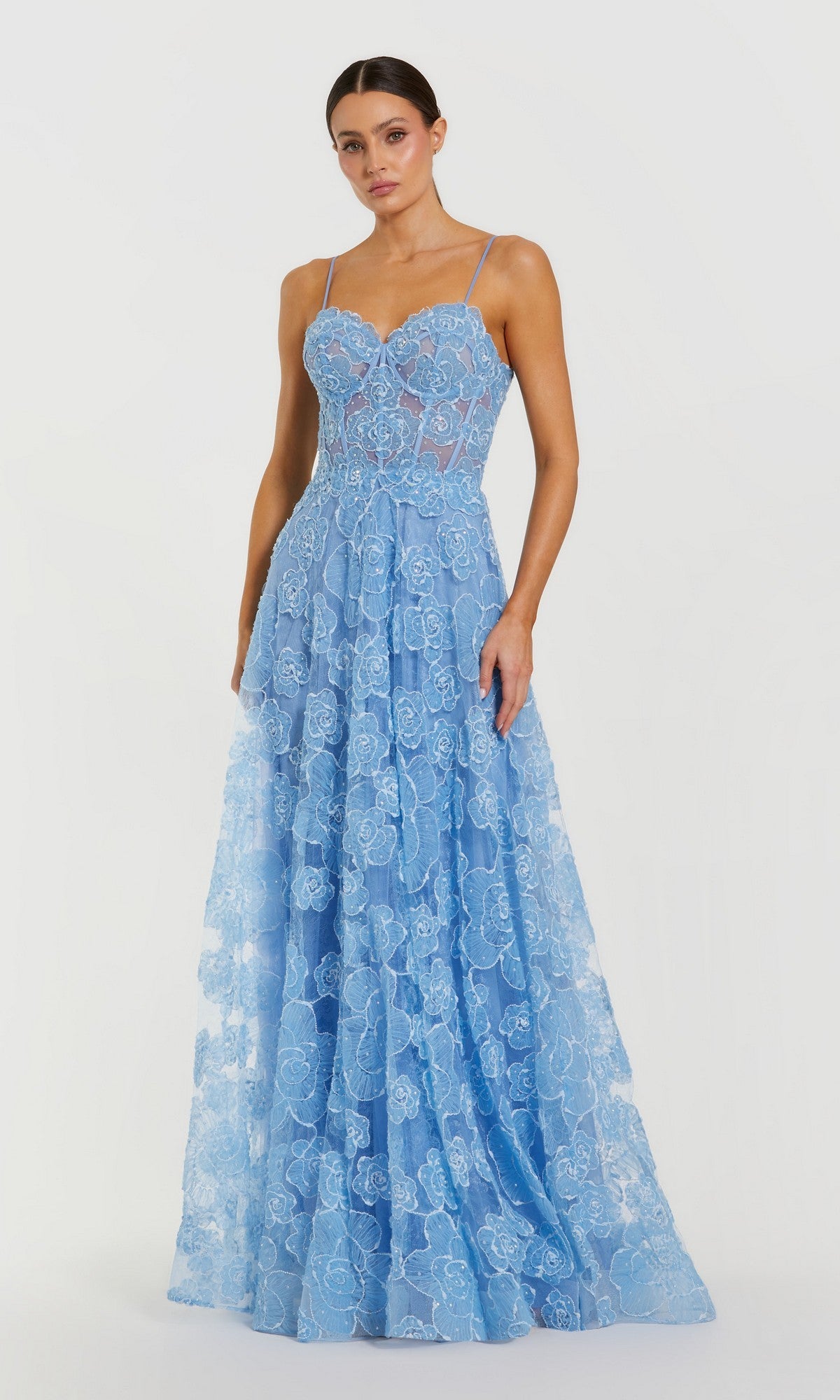 A woman wears the Mac Duggal 50735 Long Formal Dress in powder blue, a floor-length, sleeveless lace gown with thin straps and a floral pattern, standing against a plain white background.