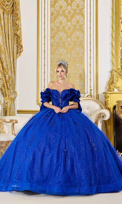 Wearing the Quinceanera Dress 5080 By Dancing Queen in royal blue, a woman with a crown sits on an ornate white and gold sofa in an opulent gold room.