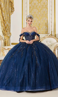 A woman wearing the Quinceanera Dress 5083 by Dancing Queen in navy and a tiara poses gracefully in an ornate room with gold and cream decor, standing in front of an elegant sofa.