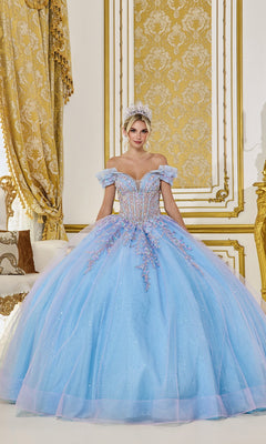 A woman stands in an ornate room wearing the Quinceanera Dress 5084 by Dancing Queen in lilac/Bahama blue with sparkling embellishments and a tiara.