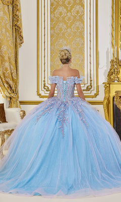 A woman in the Quinceanera Dress 5084 by Dancing Queen, an ornate blue off-the-shoulder gown, stands with her back to the camera in an opulent, gold-decorated room.