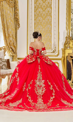 A woman wearing the Quinceanera Dress 5086 By Dancing Queen, featuring red fabric, gold embroidery, and a lace-up corset, stands with her back to the camera in an ornate gold-decorated room.