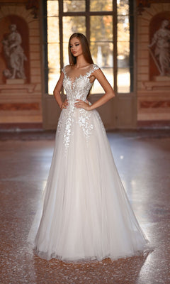 A woman wearing the Alyce 5090 long formal dress, featuring lace embroidery and an a-line tulle skirt, stands in a sunlit room with classical statues and large windows.