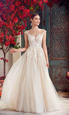A woman in the Alyce 5090 long formal dress in ivory/champagne, featuring lace embroidery and an a-line tulle skirt, stands near a vintage blue door with red flowering plants.