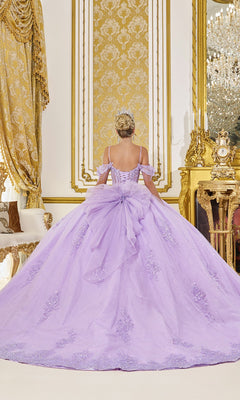 A woman in the Quinceanera Dress 5093 by Dancing Queen, featuring lilac purple glitter tulle and sequin lace appliqué, stands facing a gold ornate wall in a luxurious, decorated room.