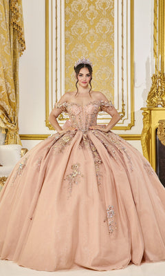 A woman wearing the Quinceanera Dress 5097 By Dancing Queen in rose gold, featuring an off-the-shoulder design and embellished corset bodice with a tiara, stands in an ornate room adorned with gold and cream curtains and matching wall paneling.