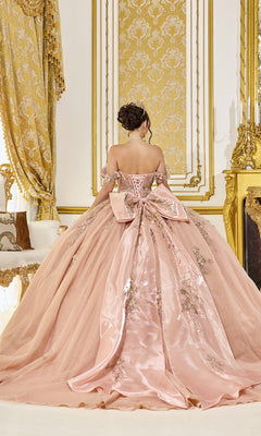 A woman wearing the Quinceanera Dress 5097 by Dancing Queen—a pink off-the-shoulder gown adorned with floral embroidery, an embellished corset bodice, and a dramatic back bow—stands in an ornate room accented with gold decor.