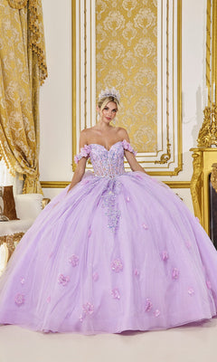 A woman in the Quinceanera Dress 5098 by Dancing Queen, a lilac gown with a sheer corset bodice and 3D flower embellishments, stands in an ornate gold-accented room, her look finished with a sparkling tiara.