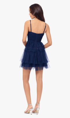 A woman faces away, wearing the Cut-Out Short Ruffled Homecoming Dress 5098BN in navy blue with thin straps, a ruched sweetheart bodice, tiered tulle skirt, and white high-heeled sandals.
