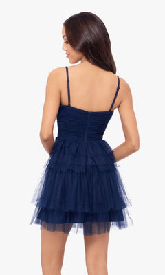A woman stands facing away, wearing the Cut-Out Short Ruffled Homecoming Dress 5098BN: a navy blue sleeveless A-line dress with spaghetti straps and a fitted ruched sweetheart bodice.