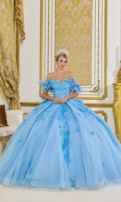 Wearing the Quinceanera Dress 5103 by Dancing Queen in Bahama Blue, a woman stands in an ornate gold and white room, smiling at the camera. The ballgown features a tulle skirt and delicate 3D floral appliques.