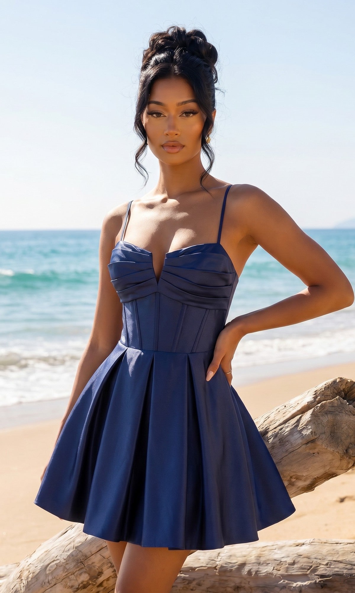 A woman in the Lace-Up Short Hoco Dress: Blondie Nites 5107BN in cadet blue stands by a driftwood log on a sandy beach, with the ocean and blue sky in the background.
