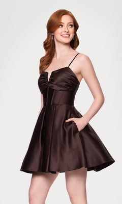 A woman with long red hair wears the Blondie Nites 5107BN Lace-Up Short Hoco Dress—a sleeveless, dark brown satin mini dress with thin straps, a flared skirt, and chic lace-up back—standing with one hand in her pocket.