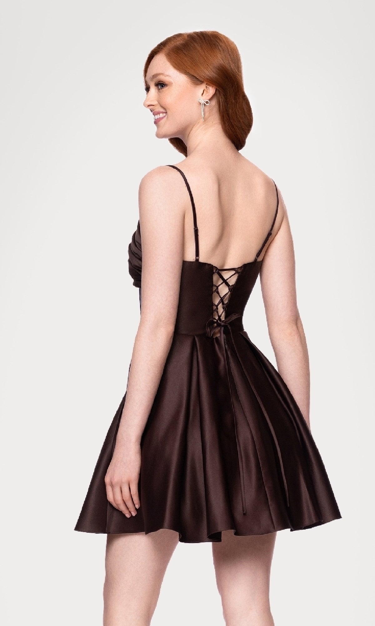 A woman stands smiling, facing away from the camera, in an affordable dark brown Blondie Nites 5107BN Lace-Up Short Hoco Dress featuring a sleeveless design and lace-up back.