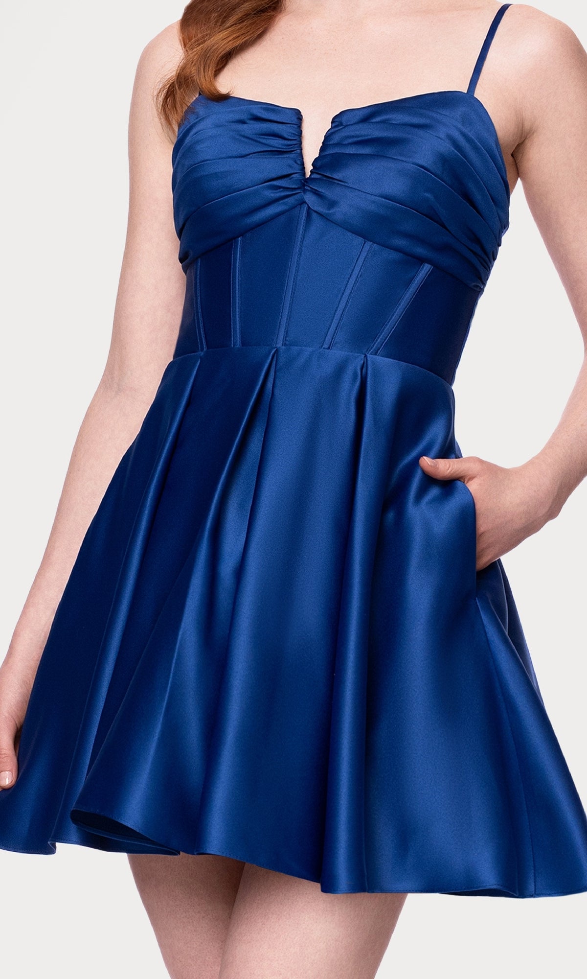 A woman in the Lace-Up Short Hoco Dress: Blondie Nites 5107BN—an affordable, deep blue satin party dress with a fitted bodice, ruched bust, flared skirt, sleeveless design, and elegant lace-up back.
