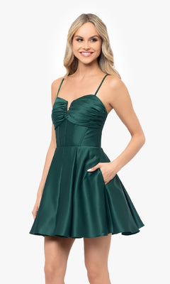A woman wears the Blondie Nites 5107BN Lace-Up Short Hoco Dress—a sleeveless, dark green satin mini with spaghetti straps and a fitted, ruched bodice—standing against a plain background.