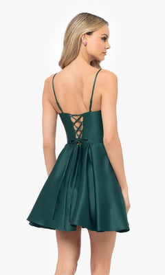 A woman in the Blondie Nites 5107BN Lace-Up Short Hoco Dress, a sleeveless dark green corset fit with a lace-up back and flared skirt, stands against a plain background.