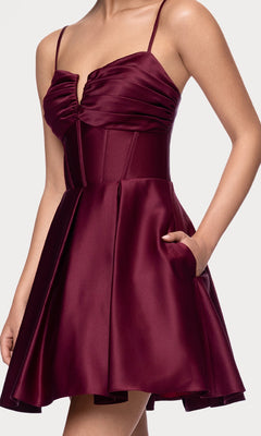 A woman models the affordable Lace-Up Short Hoco Dress: Blondie Nites 5107BN—a sleeveless, fitted burgundy satin party dress with a flared skirt and pockets, shown from shoulders to mid-thigh.