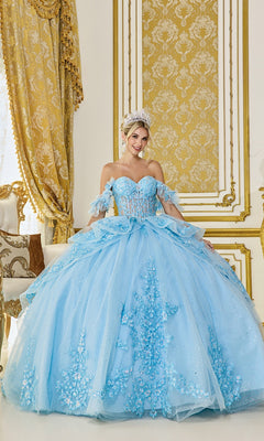 A woman in the Quinceanera Dress 5120 By Dancing Queen in Bahama Blue, featuring floral lace applique and a tiara, poses in an elegant room with gold-accented white furniture and drapes.