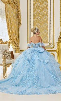 A woman in the Quinceanera Dress 5120 By Dancing Queen, a stunning light blue ball gown with floral lace applique, stands with her back to the camera in an ornate gold and white room with luxurious curtains and furniture.