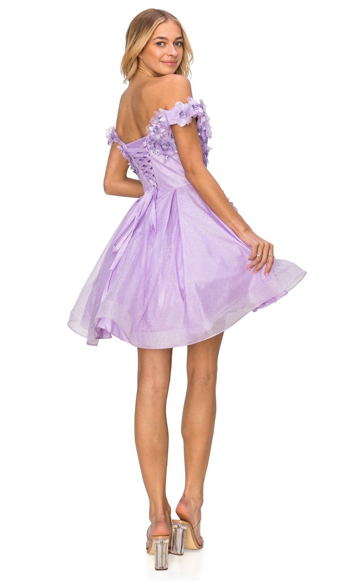 A woman wears the Shimmer Off-Shoulder Short Homecoming Dress 5120J in lavender with floral details and clear high heels, looking back over her shoulder.