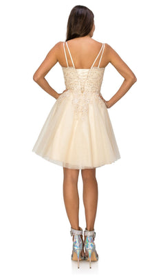 A woman stands with her back to the camera, wearing the Corset-Back Short Glitter Homecoming Dress 5125J in light beige, paired with silver holographic ankle boots.