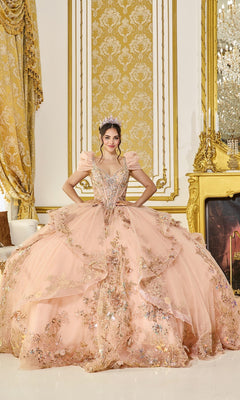 A woman wearing the Quinceanera Dress 5130 By Dancing Queen in rose gold, featuring 3D floral appliques and a sparkling tiara, stands in an opulent room with gold décor, patterned wallpaper, and a decorative fireplace.