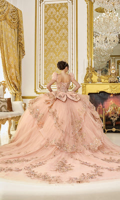Wearing the Quinceanera Dress 5130 By Dancing Queen, a person stands with their back to the camera in an opulent, gold-accented room featuring a large mirror and a sparkling chandelier. The pink gown is adorned with 3D floral appliques.