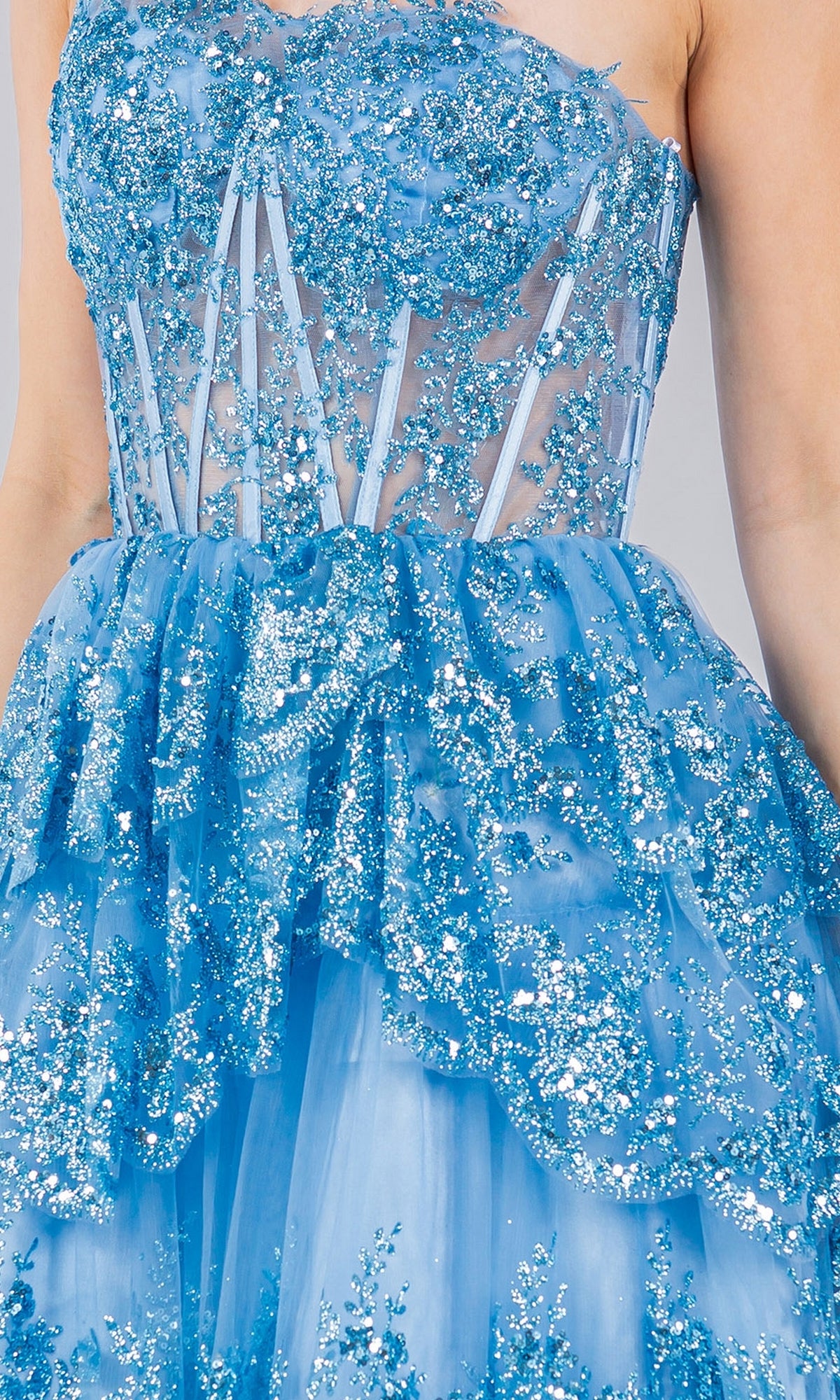 A person wearing the One-Shoulder Short Tiered Homecoming Dress 5132J, featuring a sheer blue design with sparkling sequin embellishments and layered tulle.