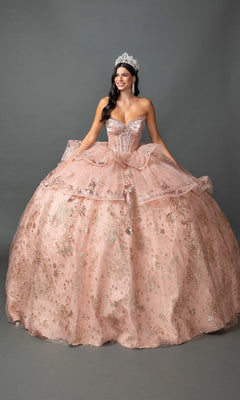 A woman wearing a silver tiara and the Quinceanera Dress 5133 by Dancing Queen in shimmering rose gold stands smiling against a plain gray background. The strapless ballgown features a beaded corset bodice, adding an elegant touch to her radiant look.