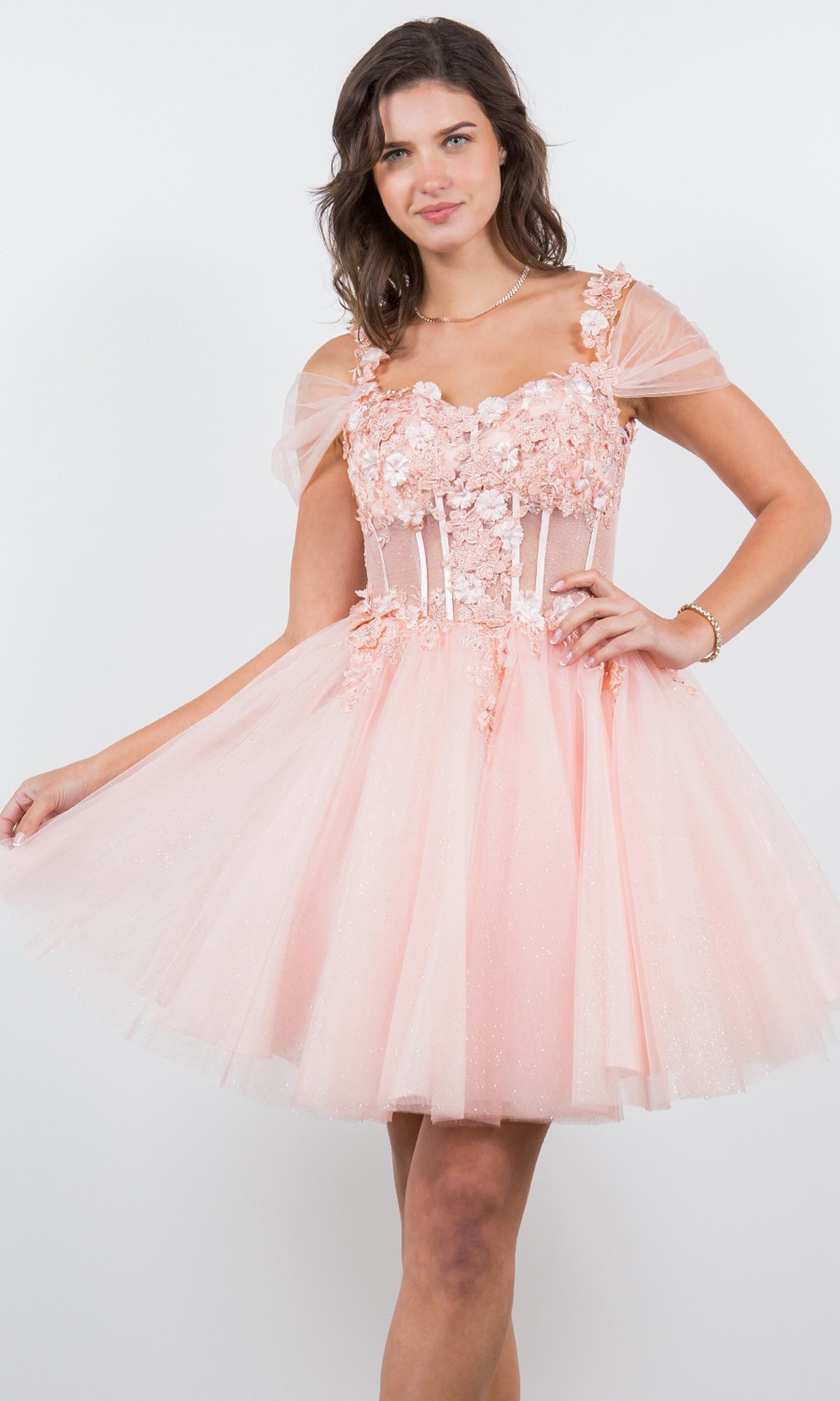 A woman wears the Embellished Short Glitter-Tulle Homecoming Dress, featuring light pink floral appliqué and sheer cap sleeves, standing against a plain white background.