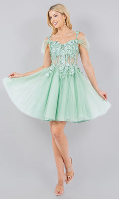 Woman modeling the Embellished Short Glitter-Tulle Homecoming Dress, a light green off-shoulder style with sheer floral details, against a plain light gray background.