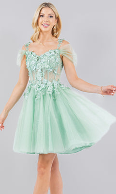 A woman wears the Embellished Short Glitter-Tulle Homecoming Dress, featuring a fit-and-flare silhouette in light green with floral appliqué and sheer sleeves, standing against a plain gray background.