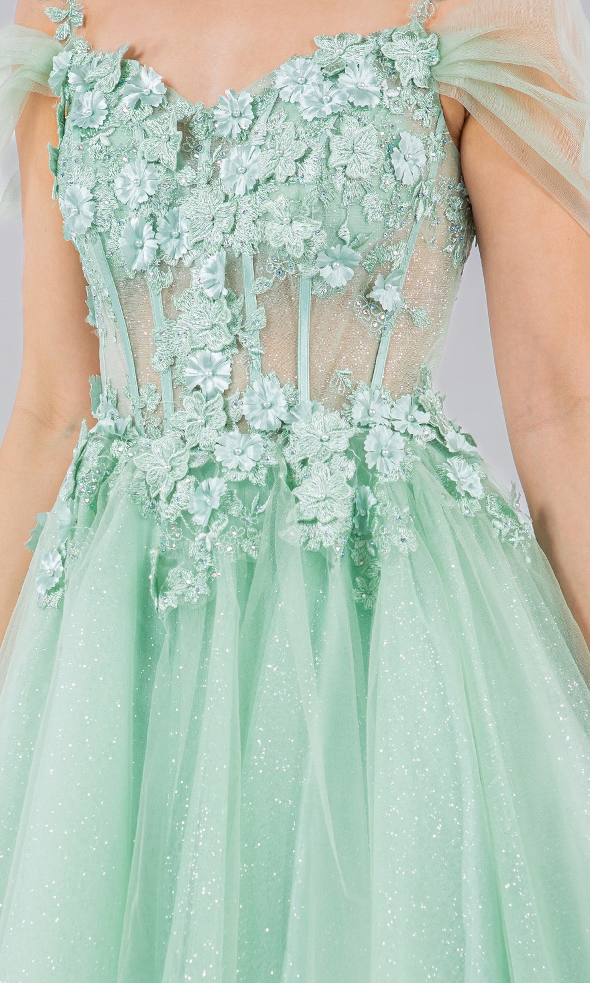 A close-up of the Embellished Short Glitter-Tulle Homecoming Dress in mint green, featuring floral appliqué, sheer bodice panels, off-shoulder tulle sleeves, and a sparkly tulle skirt.