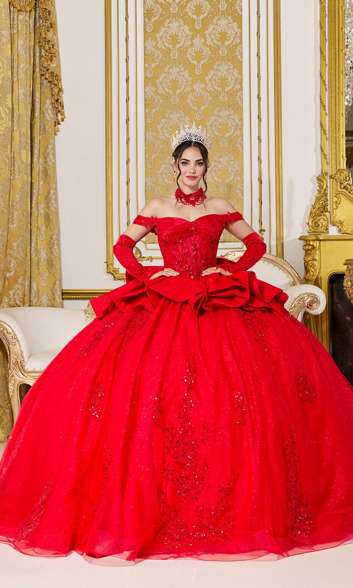A woman wearing the Quinceanera Dress 5138 by Dancing Queen in red, along with gloves and a tiara, sits on a cream and gold sofa in an ornate, gold-accented room.