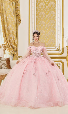 Wearing the Quinceanera Dress 5145 By Dancing Queen in blush, a woman with a tiara stands indoors against ornate gold and white décor.