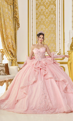 A young woman in the blush Quinceanera Dress 5152 by Dancing Queen, featuring a sparkling corset bodice and tiara, stands smiling at the camera in an ornate room adorned with gold and white decor.