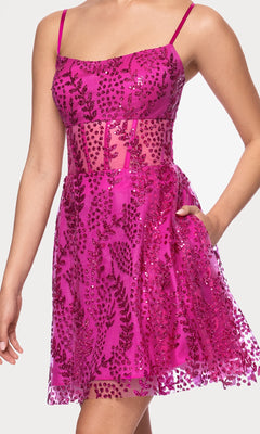 A person wearing the Blondie Nites 5153BN Short Glitter Hoco Dress, a sleeveless hot pink cocktail dress with thin straps, sequin leaf patterns, and a semi-sheer midsection.