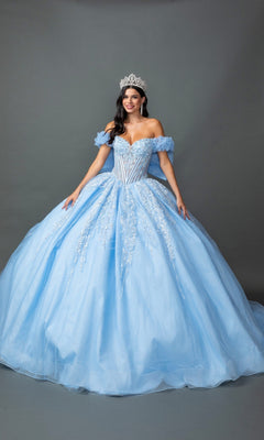 A woman wears the Quinceanera Dress 5160 By Dancing Queen in Bahama Blue, featuring a corset bodice, off-shoulder design, voluminous skirt with intricate beading, and a silver tiara. She stands against a plain gray background.
