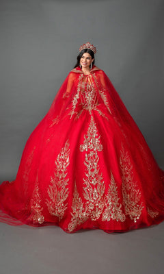A woman is wearing the Quinceanera Dress 5161 by Dancing Queen—a stunning bright red strapless ballgown with gold embroidered appliques—paired with a matching red cape and a red tiara, standing against a plain gray background.