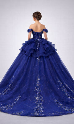 A woman with an elegant updo hairstyle wears the Quinceanera Dress 5165 By Dancing Queen, a stunning off-the-shoulder, floor-length navy-blue gown embellished with glitter and delicate floral lace appliques. She is facing away from the camera.