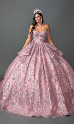 A woman wearing the Quinceanera Dress 5169 by Dancing Queen in Dusty Pink—with a sparkling beaded corset bodice and ballgown skirt—stands against a gray background, holding the sides of her dress and smiling at the camera.